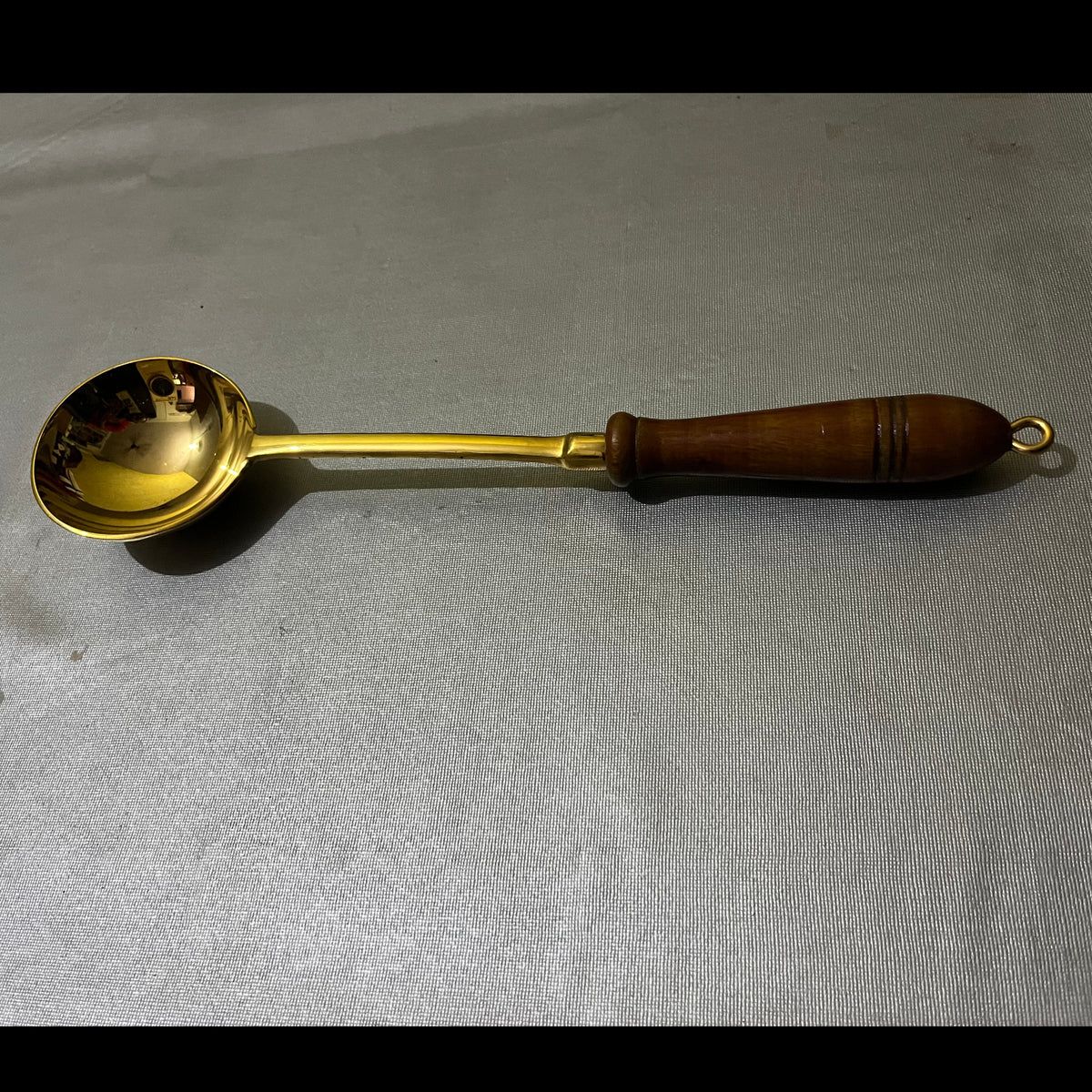A brass ladle with a dark brown wooden handle,