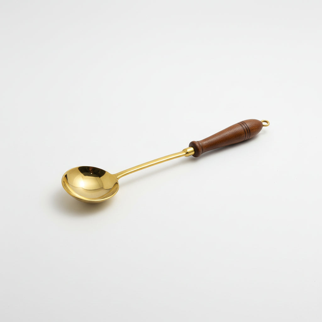 A brass ladle with a dark brown wooden handle, resting on a gray fabric surface.