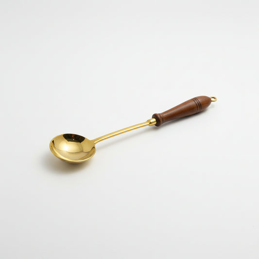 A brass ladle with a dark brown wooden handle, resting on a gray fabric surface.