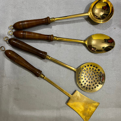 Four brass kitchen utensils with dark brown wooden handles, including a ladle, spoon, strainer, and spatula, 
