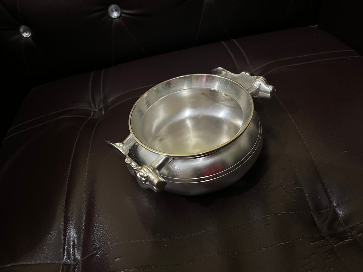 Side perspective of round silver coated brass handi bowl showing sculpted tiger motif handles