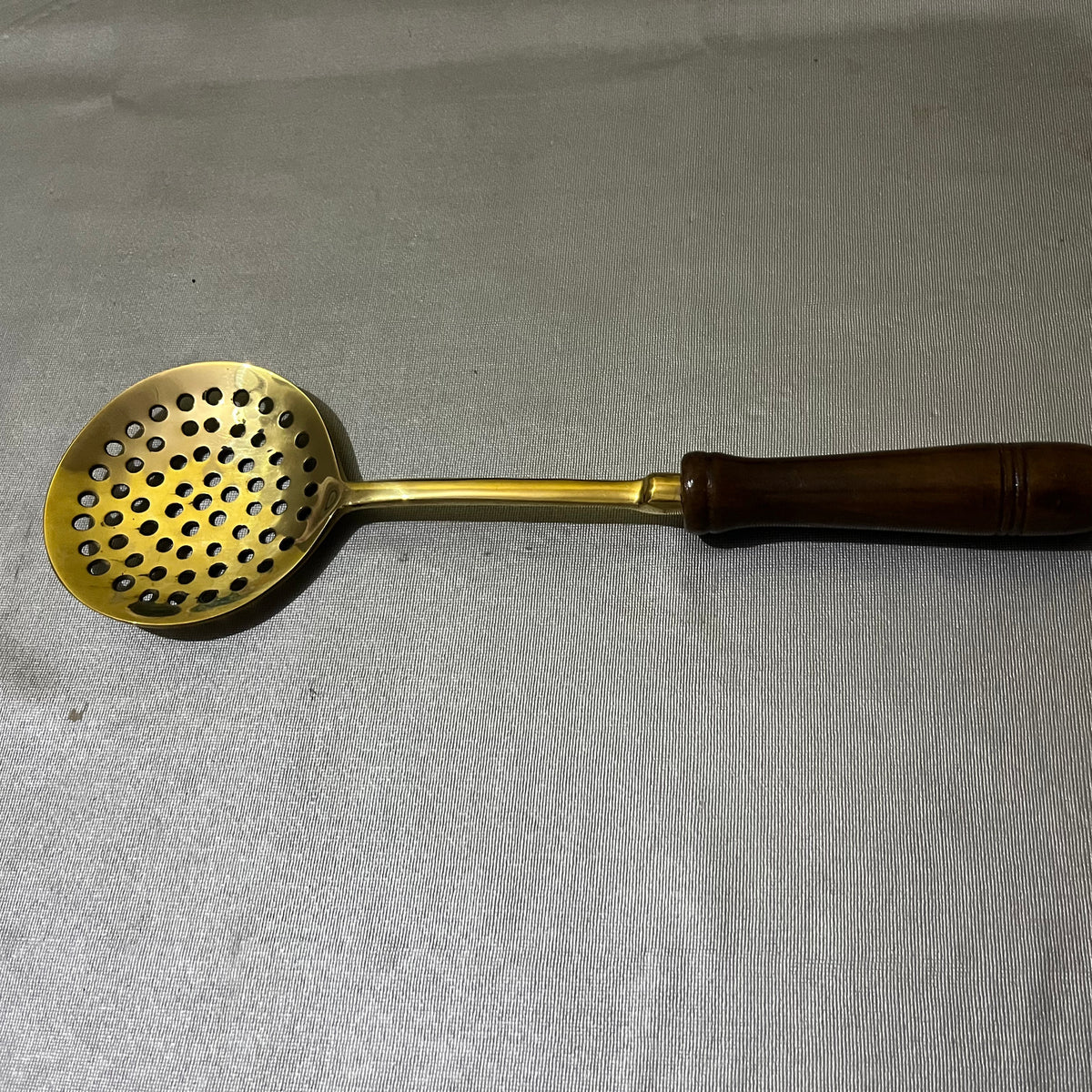 brass slotted ladle with a dark brown wooden handle.